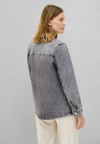 Giacca in denim grigia con un fit rilassato, polsini con bottoni e cuciture visibili. Tessuto leggermente sbiadito e design del colletto classico.