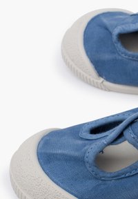 Scarpe di tela blu con suola in gomma testurizzata, dotate di due aperture a taglio e design con lacci. Tessuto morbido con dettagli bianchi a contrasto.