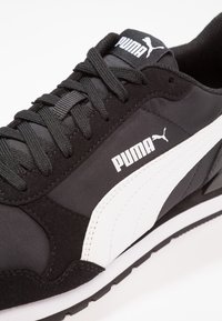 Zapatilla deportiva negra con parte superior de ante y malla, acentos blancos, logo de Puma prominente y suela texturizada para mayor agarre.