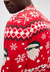 Roter gestrickter Weihnachtspullover mit weißen und grünen Mustern, darunter Schneeflocken und ein Santa-Design mit Sonnenbrille. Weiche Textur.