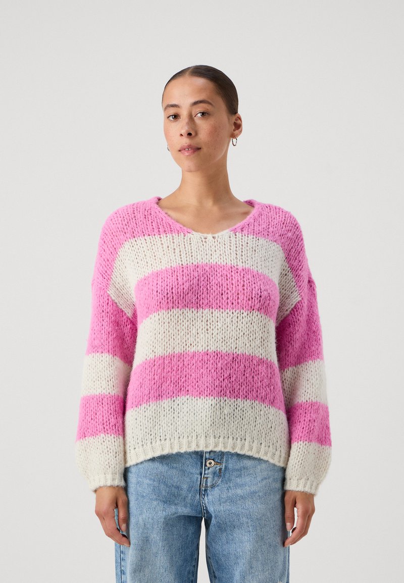 Maglione a righe rosa e bianche, con scollatura a V, vestibilità ampia, maniche lunghe e orlo a costine. Indossato con jeans azzurri a vita alta.