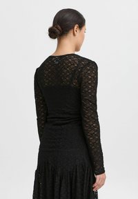 Top in pizzo nero a maniche lunghe, con un corpino aderente decorato da intricate fantasie floreali, scollatura tonda e maniche testurizzate.