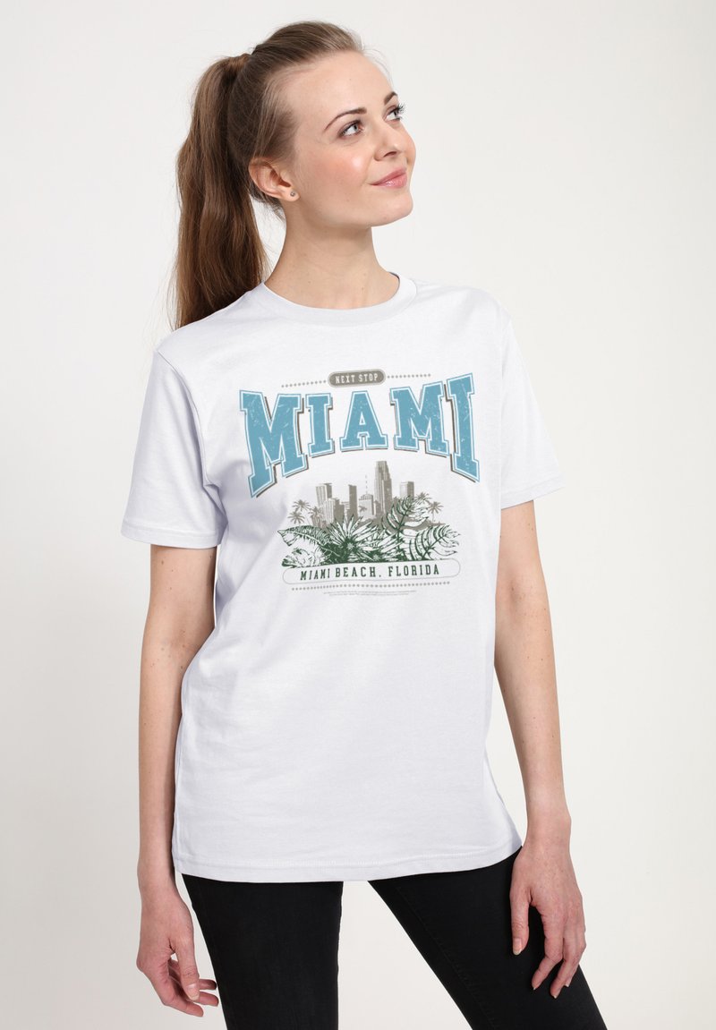 Hvid T-shirt med korte ærmer med et Miami-motiv i blå og grå med palmeblade og byens skyline. Rund hals, lavet af bomuldsmateriale.