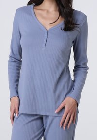 Top a maniche lunghe a coste di un morbido blu con scollatura a V e patta con tre bottoni; si abbina a pantaloni coordinati per un look rilassato.