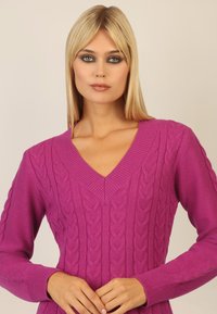 Fuchsiasweater mit V-Ausschnitt, ausgestattet mit strukturierten Kabelstrickmustern auf der Vorderseite und gerippten Bündchen. Glatte Stoffoberfläche.