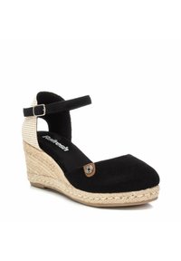 Espadrilles de cuña de ante negro con un tacón trenzado, correa al tobillo y una etiqueta decorativa marrón en la punta. Textura suave con forma redondeada.
