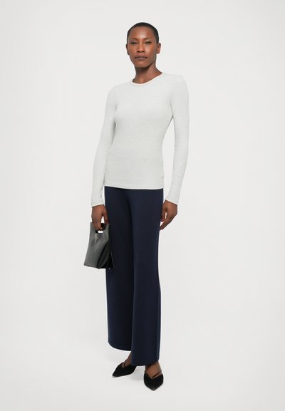 Light gray ribbed long-sleeve top paired with navy wide-leg trousers. Black handbag with a handle, and black pointed-toe flats.