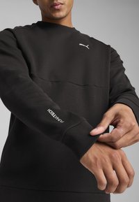 Hanorac negru cu panou superior texturat. Prezintă manșete riblate și un logo alb Puma pe piept și pe mânecă. Finisaj din material moale.