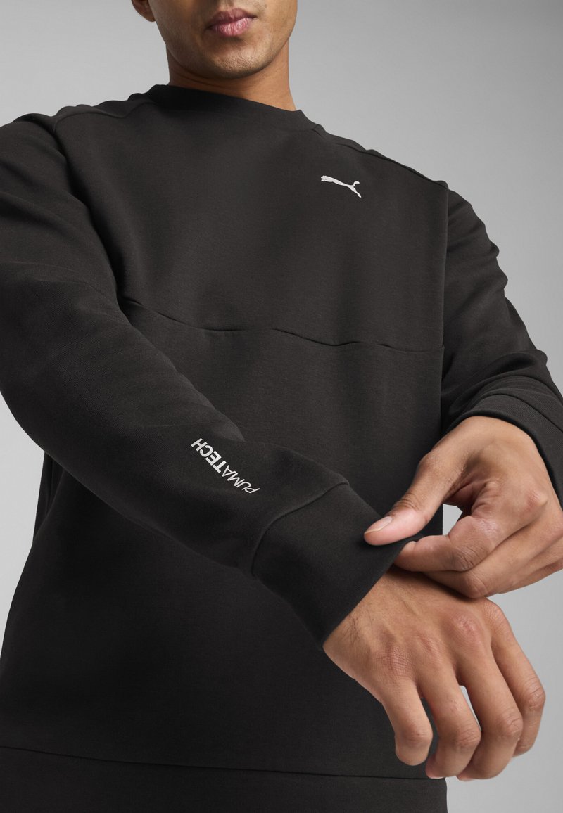 Sweatshirt noir avec panneau supérieur texturé. Présente des poignets côtelés et un logo Puma blanc sur la poitrine et la manche. Fini en matériau doux.
