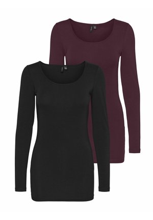 Bluză burgundy cu mânecă lungă, asociată cu blugi largi cu talie înaltă de culoare albastră și pantofi cu platformă argintii metalici, pe un fundal neutru.