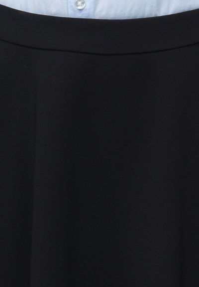 Μαύρη φούστα με φαρδύ ζωνάρι φορεμένη πάνω από ένα ανοιχτό μπλε πουκάμισο με κουμπιά, που δείχνει τη μέση και την περιοχή των γοφών.