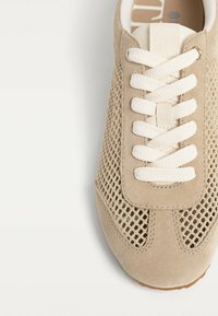 Baskets beiges avec panneaux en mesh, accents en suède et lacets blancs. Bout arrondi avec couture discrète et semelle texturée.