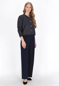 Cardigan bleumarin cu nasturi argintii și un finisaj texturat, ușor strălucitor; asortat cu pantaloni bleumarin cu croială lejeră și pantofi negri cu vârful ascuțit.