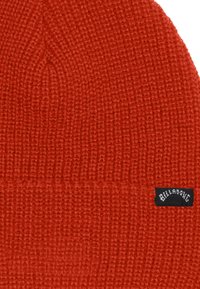 Berretto di lana rossa con motivo a trama, dotato di un'etichetta nera Billabong sul lato. Materiale morbido e forma arrotondata.