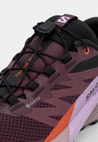 Salomon Sense Ride 5 tenisice imaju maroon sintetički gornji dio s crnim i narančastim detaljima, teksturiranu mrežicu, sustav brzog vezanja i podstavljeni potplat.