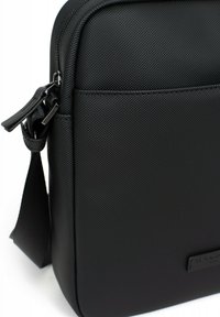 Borsa messenger nera con texture, chiusura a zip, tracolla regolabile e forma rettangolare con un discreto patch logo.