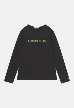 Czarna koszula z długim rękawem z dużym napisem "CALVIN KLEIN" w żółto-zielonych literach na piersi oraz małym logo "ck" na mankiecie lewego rękawa.