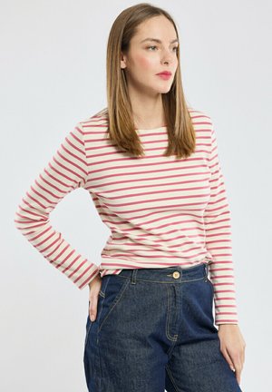 Haut à manches longues rayé en crème avec de fines rayures roses, présentant un col rond. Associé à un pantalon en denim bleu foncé taille haute.