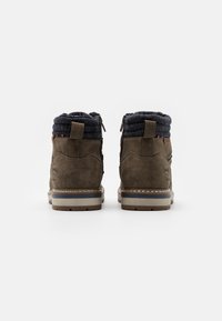 Bottes ankle marron foncé avec une finition texturée, présentant un col en tricot bleu marine, un détail de boucle à lacet et une semelle rembourrée contrastante.