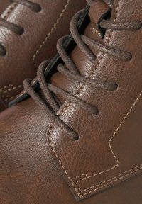 Botas de cuero marrón con superficie texturizada, cordones marrones, costuras contrastantes y un diseño de caña alta con puntera redondeada.
