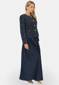 Granatowa marynarka z tkaniny tweed z złotymi guzikami w połączeniu z długą, satynową spódnicą w pasującym granacie, co tworzy skoordynowany, elegancki wygląd.