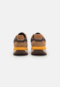 Sneakers with a combination of brown suede and navy fabric, featuring a yellow sole and grey accents. The design includes a padded collar.