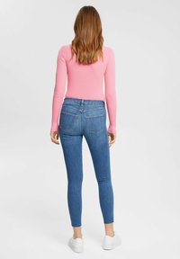 Top de manga larga de rayas rosas, combinado con jeans ajustados azules con bolsillos traseros y dobladillos deshilachados, completado con zapatillas blancas.