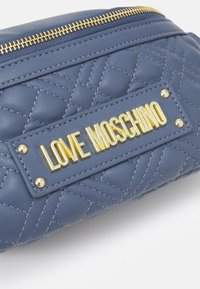 Blå kviltad läderpåse med guldzipper och guldmetallplatta med "LOVE MOSCHINO"-logotyp på framsidan.