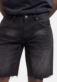 Shorts en denim noir avec un ourlet effiloché, comportant cinq poches et un léger dégradé de couleur. Fermeture à bouton en métal avec des détails de couture contrastés.