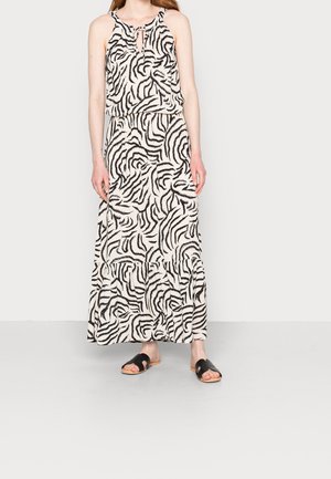Femme portant une robe maxi sans manches à imprimé zèbre noir et blanc avec un col clé et des sandales plates noires ouvertes à l'avant.