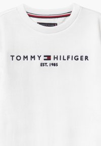 Weißes Sweatshirt mit der in Dunkelblau gestickten Aufschrift "TOMMY HILFIGER", einem kleinen roten und blauen Logo-Akzent und "EST. 1985" darunter.
