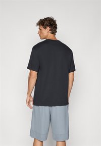 Sort kortærmet t-shirt med rund hals; afslappet pasform. Båret sammen med lysegrå shorts; synlig tekstureret stof og løs design.