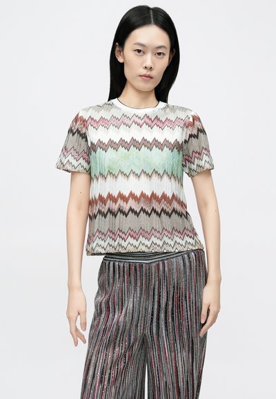 Īsroku krekls ar daudzkrāsainu zigzaga rakstu zaļu, rozā un brūnu toņu kombinācijā. Kopā ar svītrainām, teksturētām biksēm.