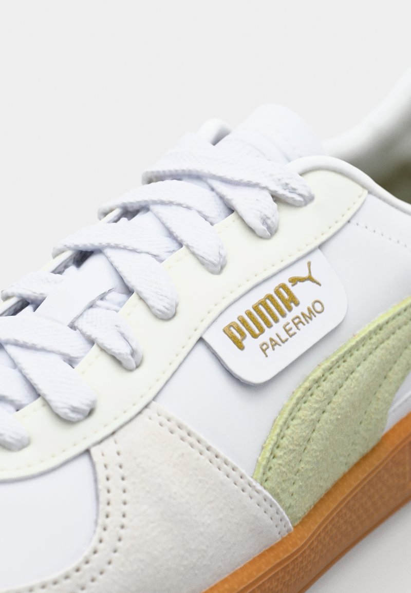 Weißer Sneaker mit hellgrünen Akzenten, Materialien aus Wildleder und Leder, flachen Schnürsenkeln und goldener Markenkennzeichnung. Gummisohle mit strukturiertem Detail.