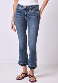 Jeans de mezclilla azul de campana con cintura alta, que cuentan con dos bolsillos frontales y un dobladillo deshilachado con costuras decorativas.
