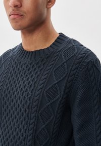 Temno mornarsko pleteno pulover z teksturiranim vzorcem, ki vključuje kabelske in diamantne oblike, ter rebrastim krožnim ovratnikom.