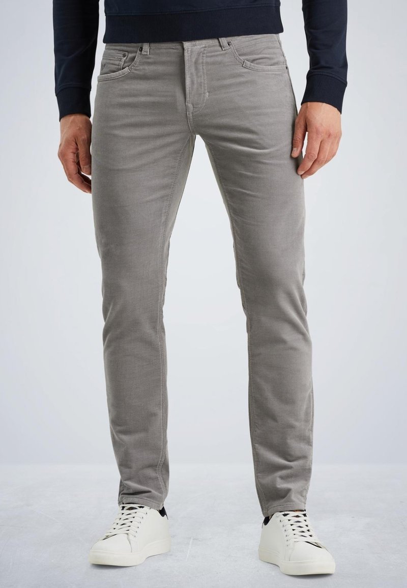 Jeans ajustados grises con cinco bolsillos y un sutil estiramiento. La textura del tejido es suave, combinados con zapatillas blancas que tienen detalles en negro.