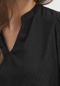 Blusa nera con scollo a V, caratterizzata da una sottile texture e dettagli plissettati sulle spalle. Il tessuto appare leggero e morbido.
