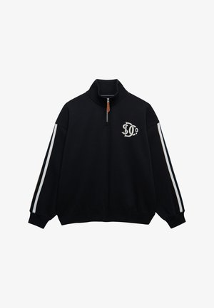 Czarna bluza z ćwiartką zamka błyskawicznego, białe paski na rękawach i biały logo na lewej piersi, z zawieszką zamka błyskawicznego z skóry.