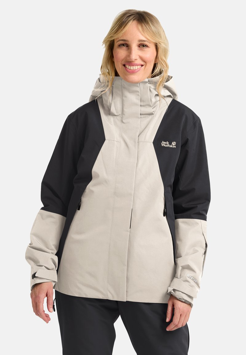 Giacca leggera e impermeabile di colore beige e nero; colletto alto, polsini regolabili, zip e dettaglio del logo sul petto; trama liscia.