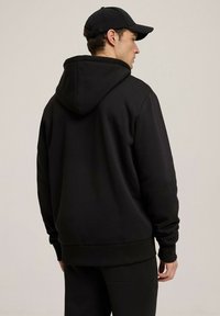 Czarna bluza z kapturem wykonana z miękkiego materiału, z kieszenią typu kangur, ściągaczami przy mankietach i u dołu oraz luźnym krojem.