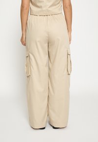 Beige cargobukser med afslappet pasform, der har sidelommer og elastisk taljebånd. Glat tekstur, bred ben-design og uden synlige mønstre.