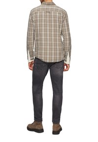 Chemise à carreaux marron et gris avec des manches longues, un empiècement au dos et des poignets boutonnés. Associée à un jean sombre et des bottes marron.