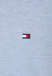 Tissu tricoté bleu clair avec un petit logo rectangulaire au centre comportant des rayures horizontales blanches, rouges et noires.