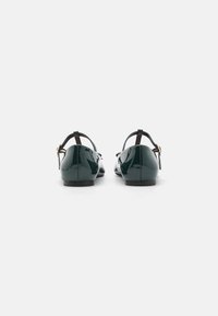 Green patent leather flats with a low heel and adjustable ankle strap. Features a smooth texture and subtle shining surface.