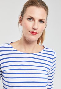 Witte langemouwen top met blauwe horizontale strepen, met een ronde halslijn en een zachte, gladde textuur. Eenvoudig ontwerp zonder patroon details.