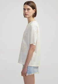 Witte katoen t-shirt met korte mouwen, voorzien van lichtbeige bloemborduursel aan de voorkant. Gepaard met denim shorts met rafelige randen.