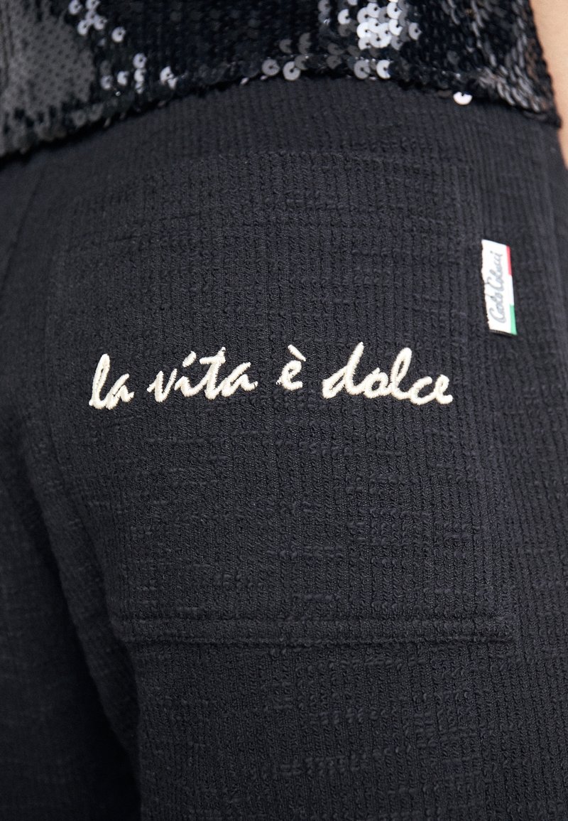 Pantalons en tissu texturé noir avec l'inscription brodée "la vita è dolce" en crème au dos, avec une petite étiquette de marque dans le coin.