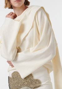 Crème oversized trui met gedrapeerd ontwerp en brede mouwen. Vloeiende structuur, gecombineerd met een bewerkte bloemdetail op een crèmekleurige rok.