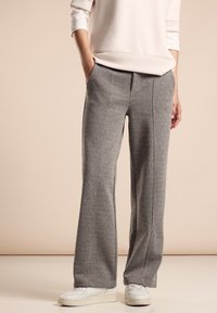 Pantalons à carreaux gris en tissu texturé, dotés d'une coupe décontractée et de plis à l'avant, associés à des baskets blanches.